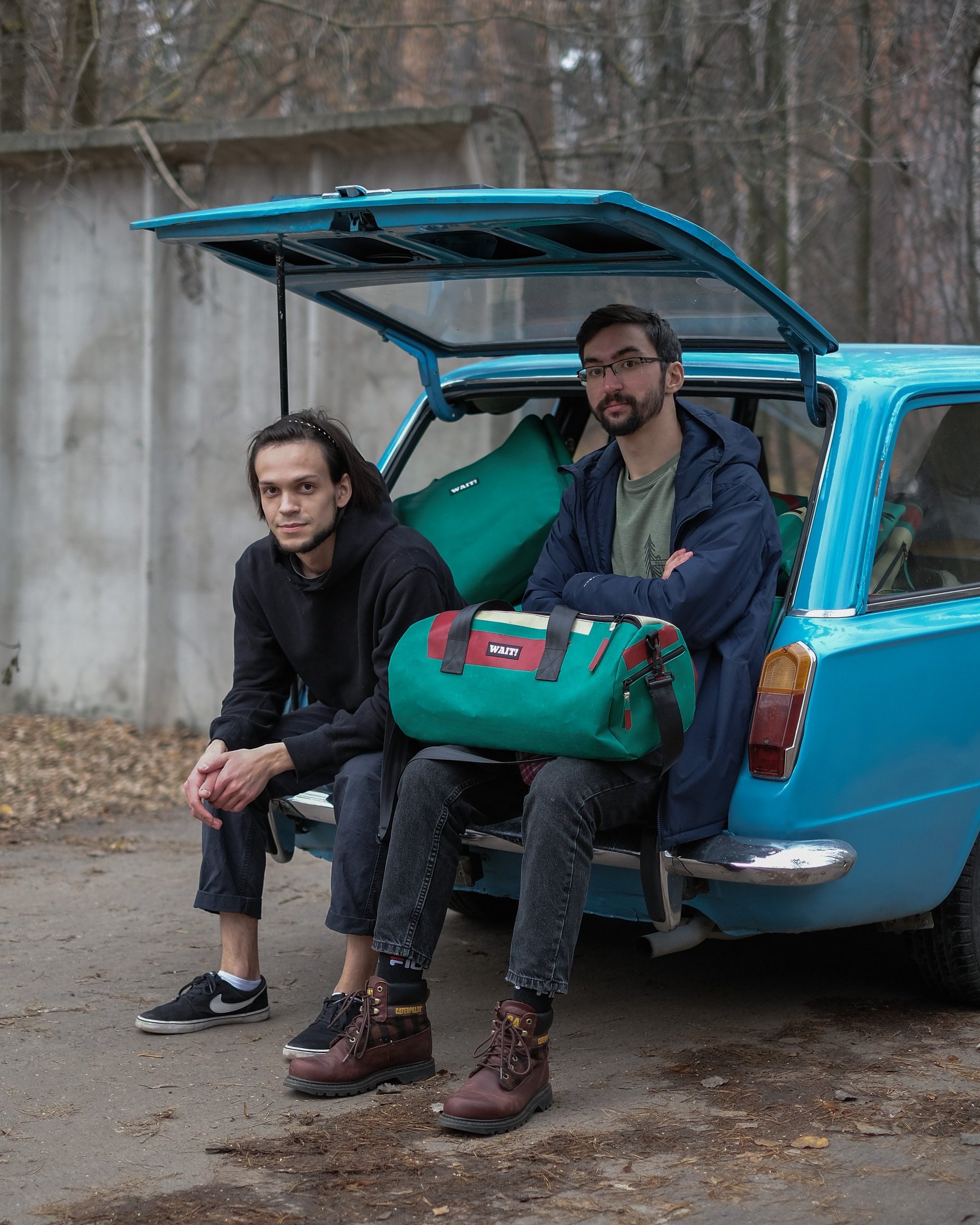 Two guys sitting on trunk of blue car